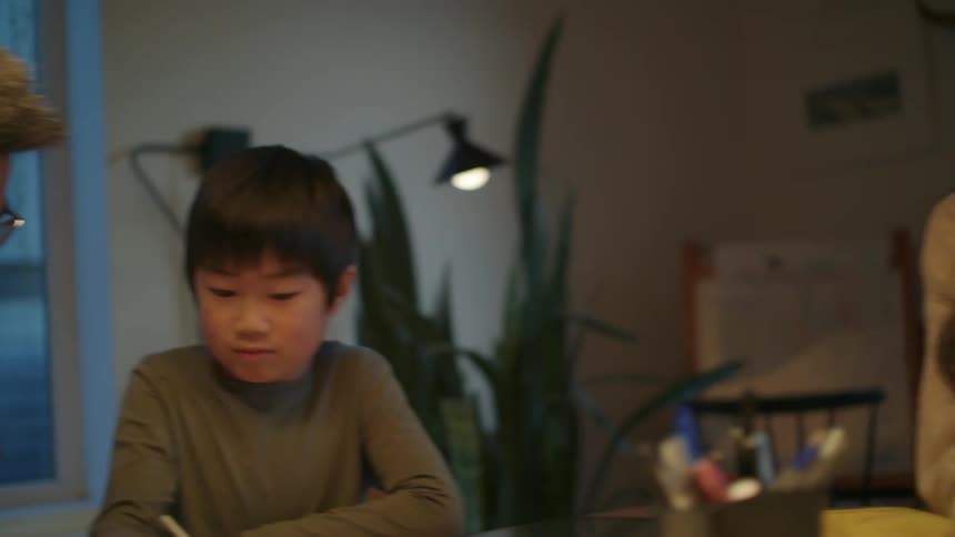 A mother and father sit with their children and help them with homework