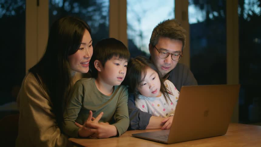 A man a woman a boy and a girl sitting at a table looking at a laptop