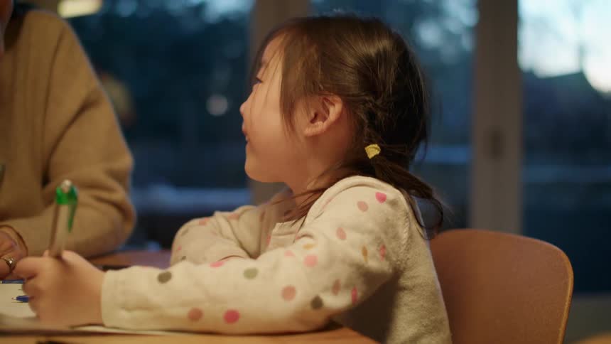 A child writing on a paper next to her mom
