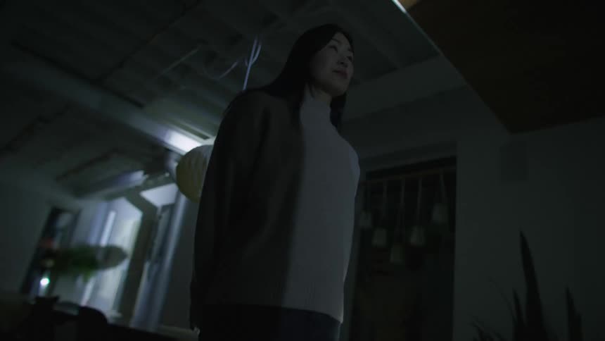 A woman stands in a room in a dark room in her home as light flash all around her