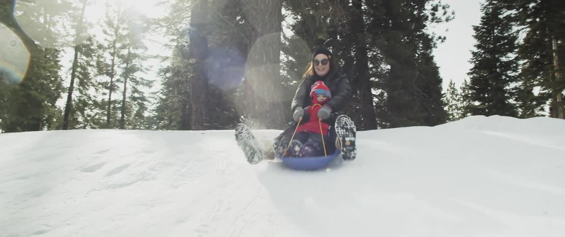 A woman and baby sledding down a snowy hill