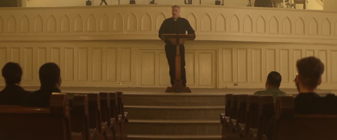 A pastor gives a sermon while standing at a lectern on a raised platform in a large church