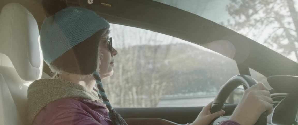 Young woman driving a car on a road next to a lake in the mountains in the morning