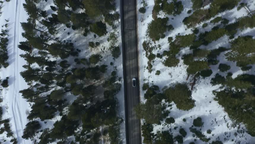Aerial view vehicle driving down a rural road through the snow covered pine tree forest