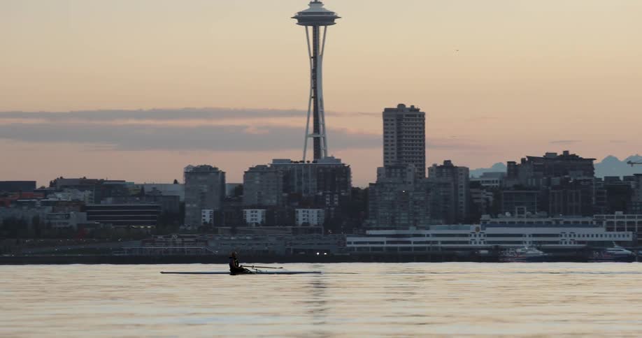 A man is rowing in the water by a city at sunset