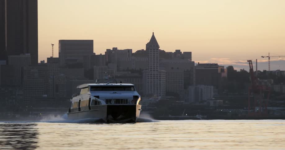 A ferry boat speeds across a harbor with a city in the background