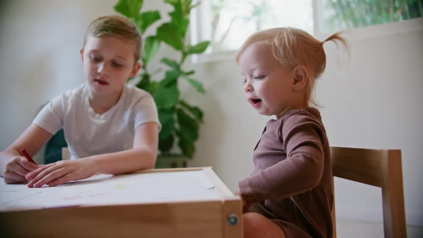 A boy and his little sister sit at home and color