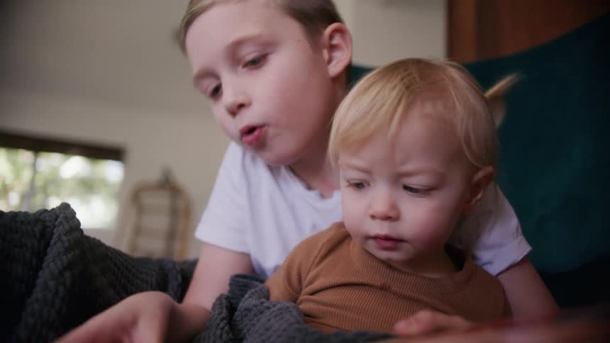 To children reading a book together on a couch