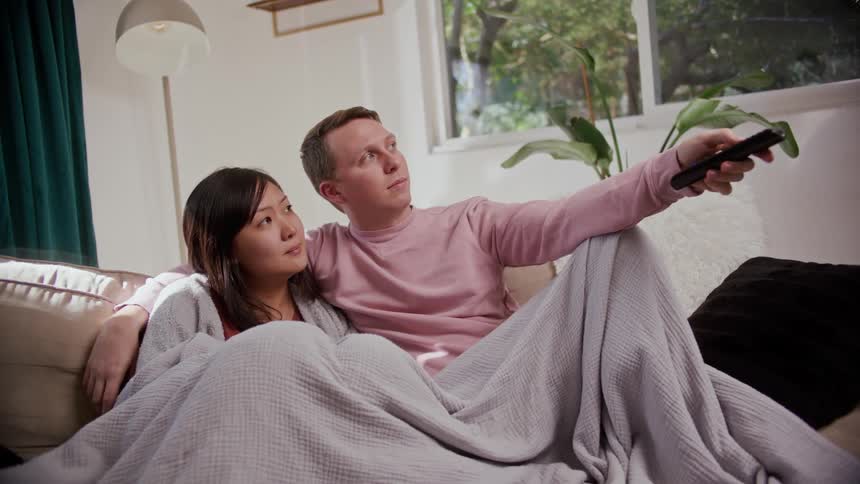 A man and woman cuddle on the couch together with a blanket