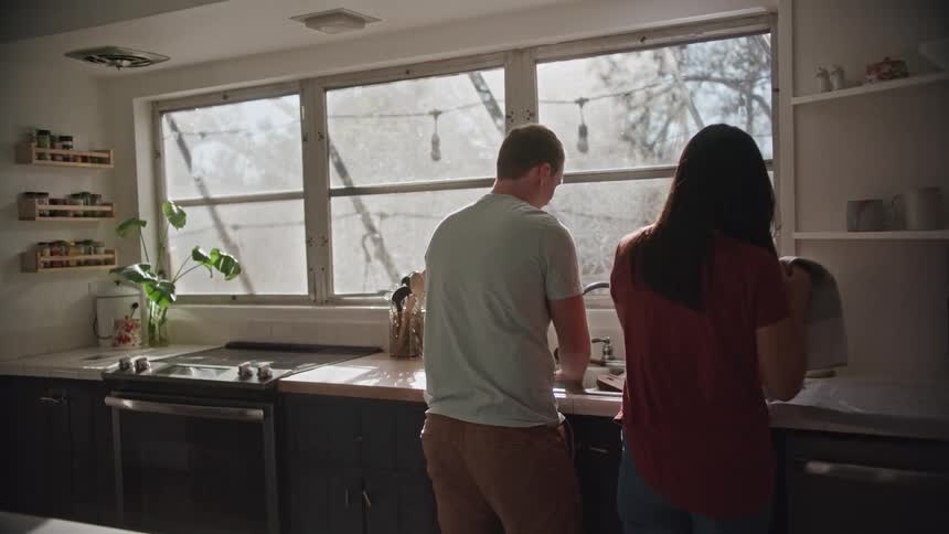 A woman hugs and kisses a man as they wash dishes