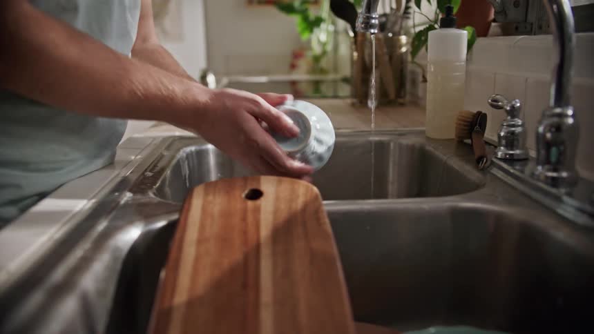 A man washing dishes in a sink in front of a window
