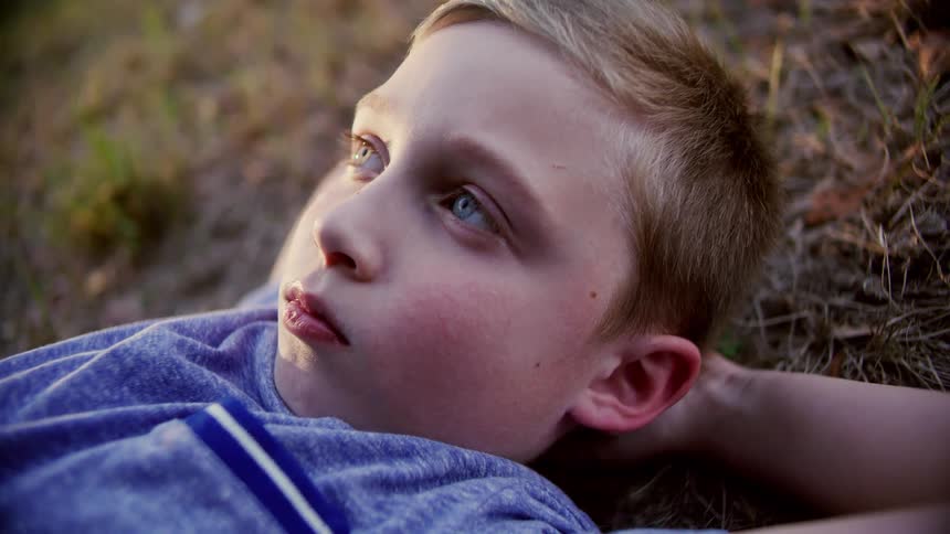 A young boy lays on his back on the grass while looking upwards