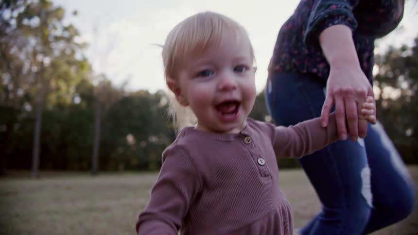 A little girl holds hands and runs with her mother in a grassy field