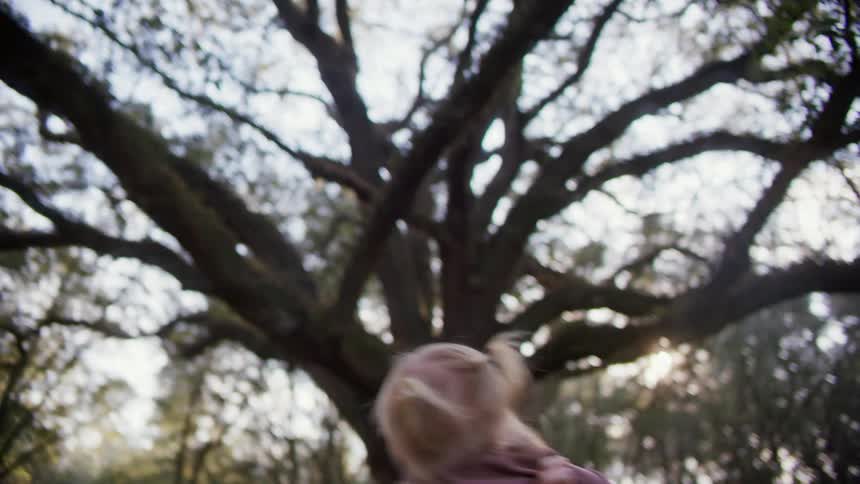 A mom holds her daughter up and twirls around with her in the yard