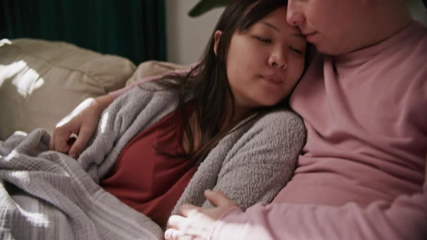 A man rubs his wifes arm as they cuddle together on a couch