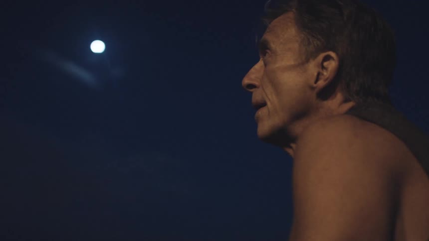 An elderly man stands outside under the moon