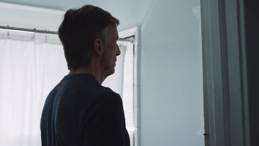 A man stands in his bathroom and looks in the mirror