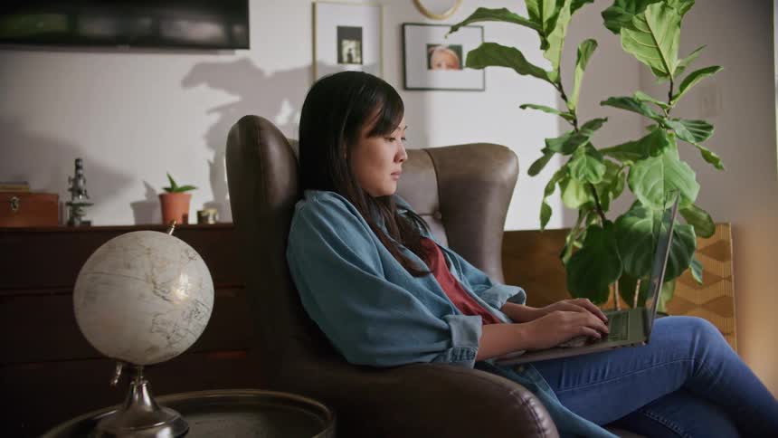 A woman in a room sitting on a couch typing on a laptop