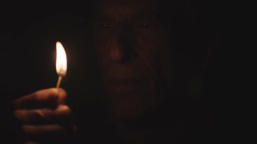 A man in the dark holding a match with fire and smoke