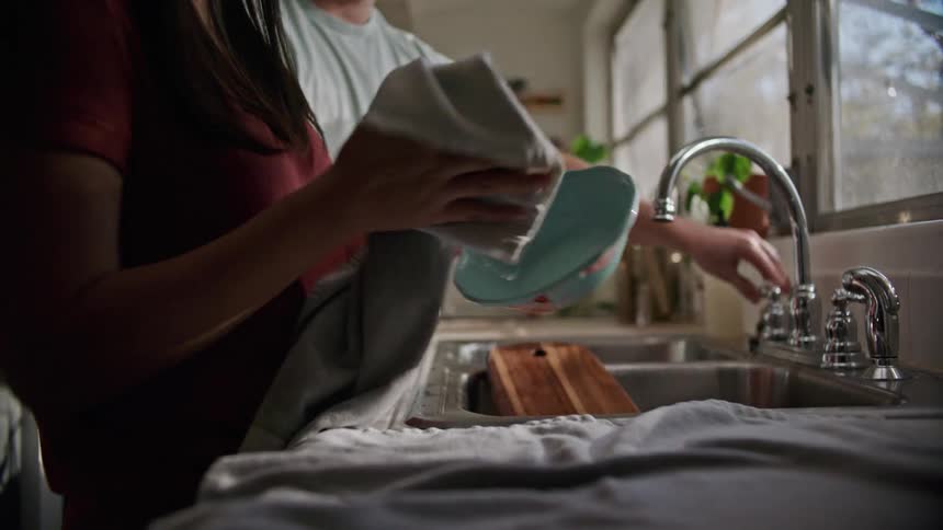 A woman dries dishes with a towel after her husband washes them