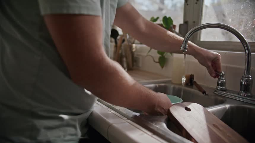 A man is doing dishes inside of his kitchen