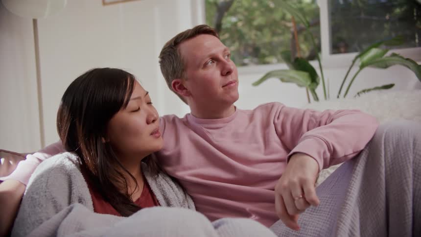 A man sits with his arm around his wife as they watch television at home