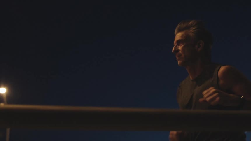 A man runs past a gas station and onto bridge at night