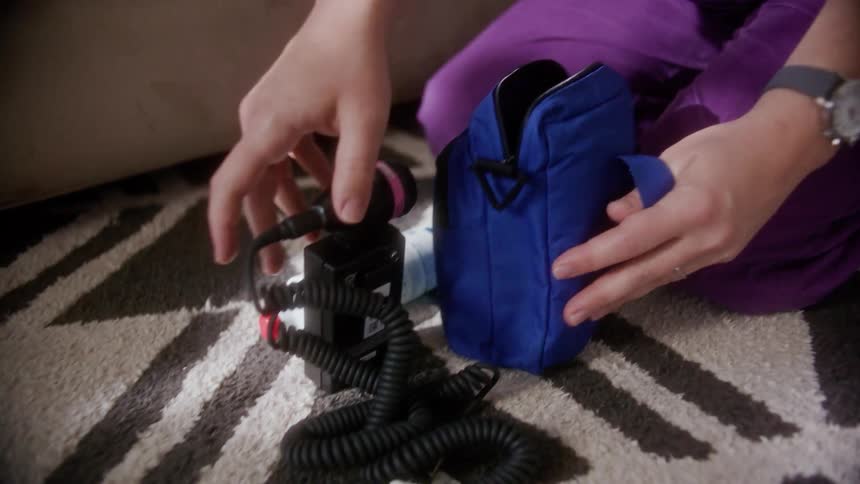 A nurse kneels on the ground in a home and removes medical equipment from a blue bag