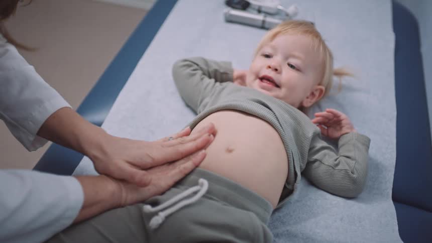 A young child lays on her back and smiles while a doctor examines her belly