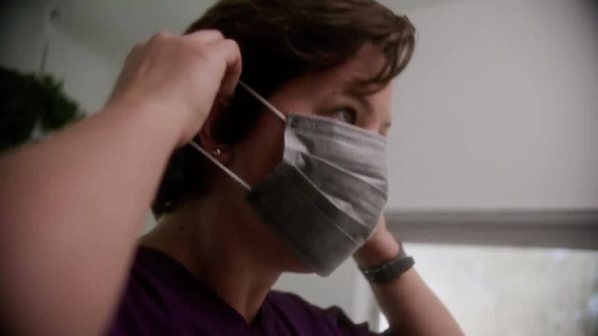 A woman picks up a disposable face mask from the bathroom counter and puts it on her face