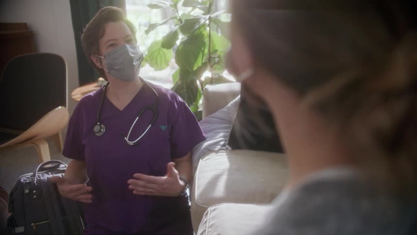 A woman talks with a nurse in the living room of a house during the day