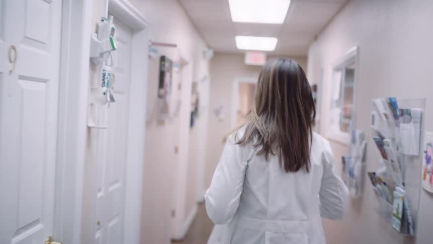 A doctor walking down a hallway and into a room in an office