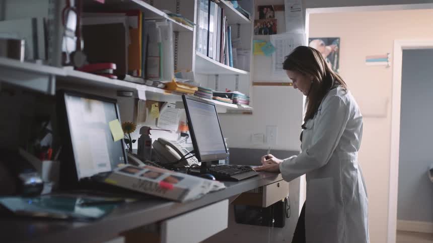 A female physician stands at a counter while writing with a pen