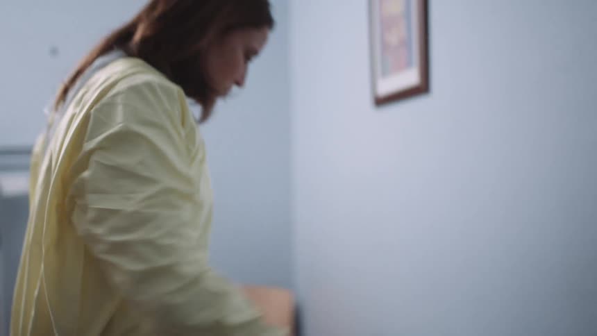 A physician quickly dons a disposable gown and face mask while in an examination room