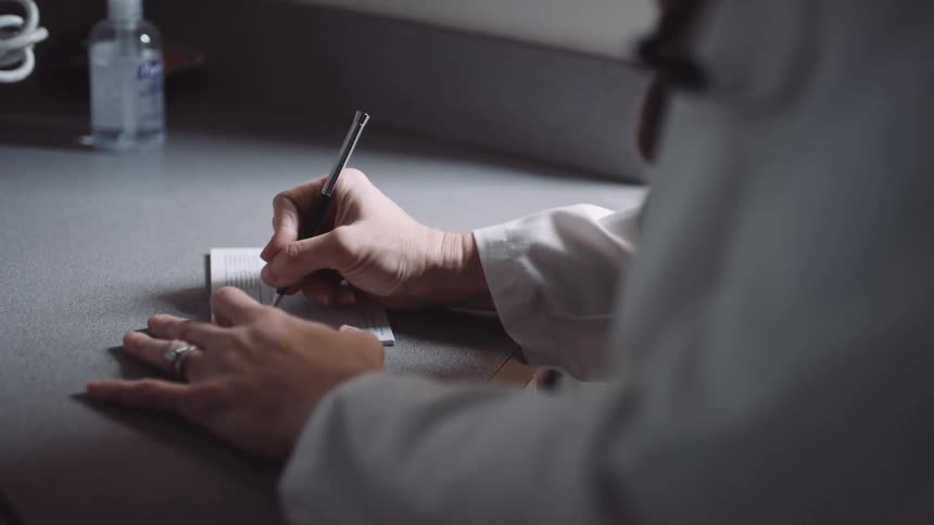 A doctor fills out a prescription on a paper pad and rips the top sheet off