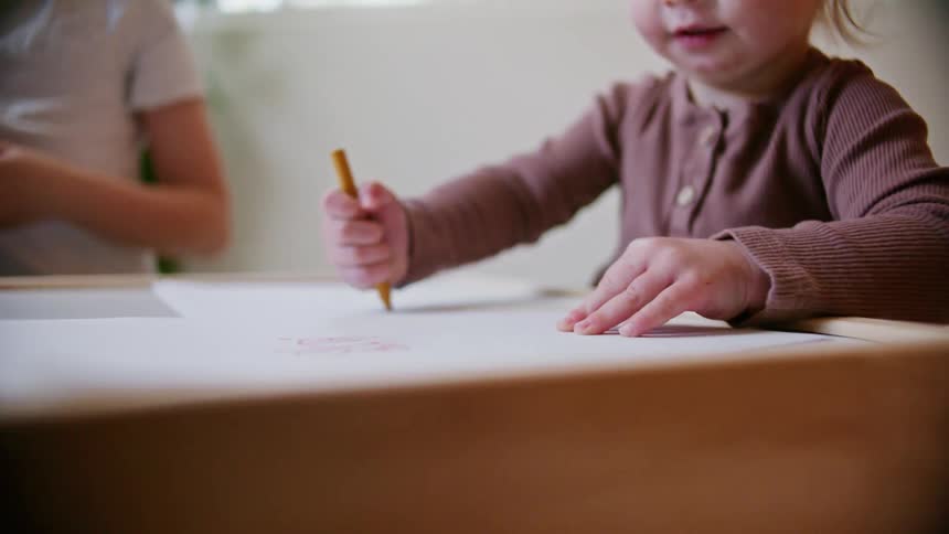 Two kids drawing with crayons on a piece of paper