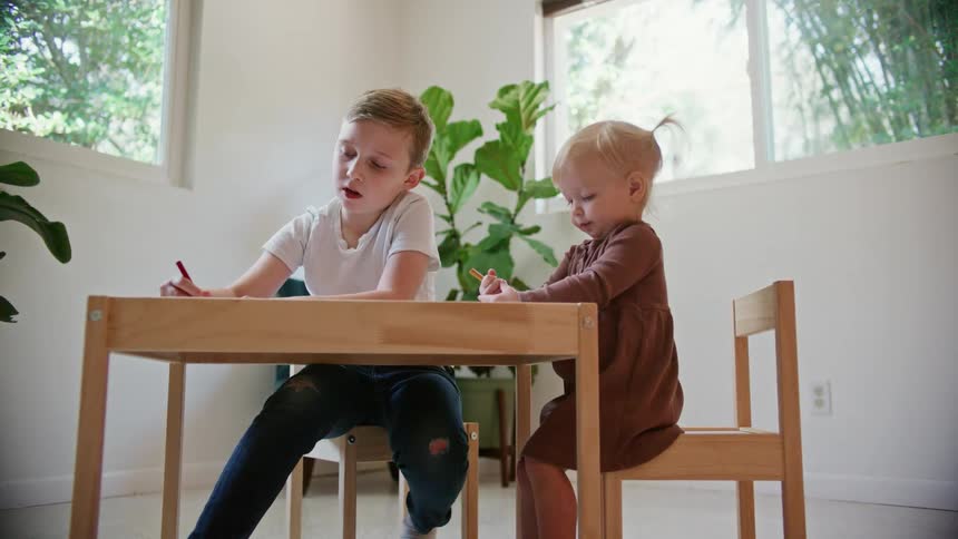 Brother and sister drawing with crayons over a table in a room at home