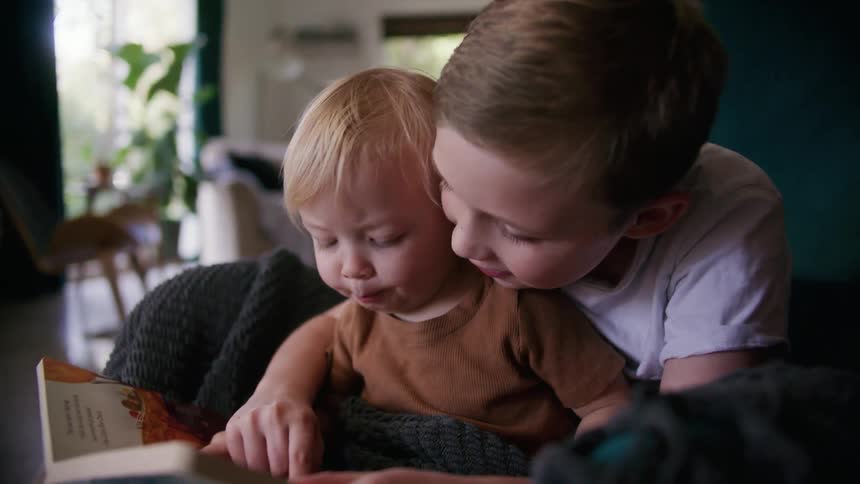 A boy smiles while reading to his younger sister as she sits in his lap