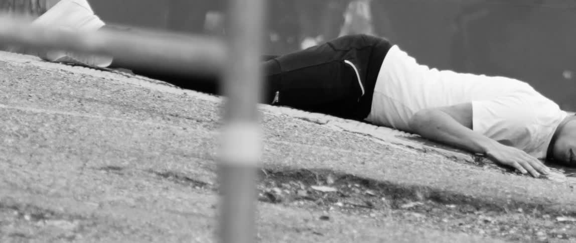 Person lying awkwardly outdoors on concrete with their eyes open