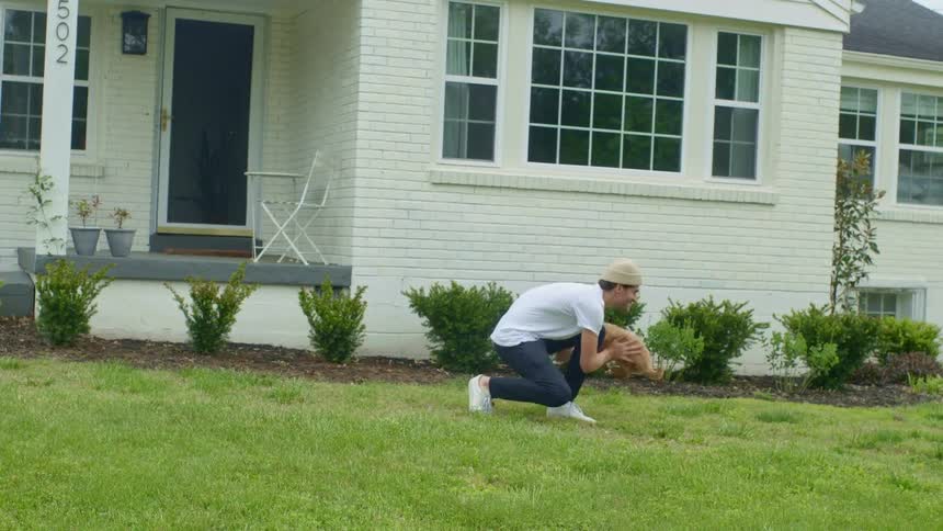 A man stands in a front yard and bends down to pick up a small puppy running towards him