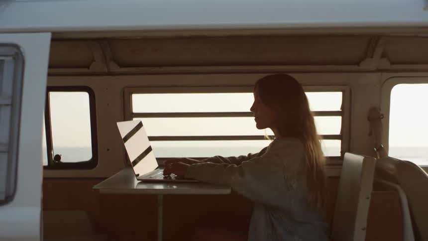 A woman in a van sitting on a chair next to a table typing on a laptop