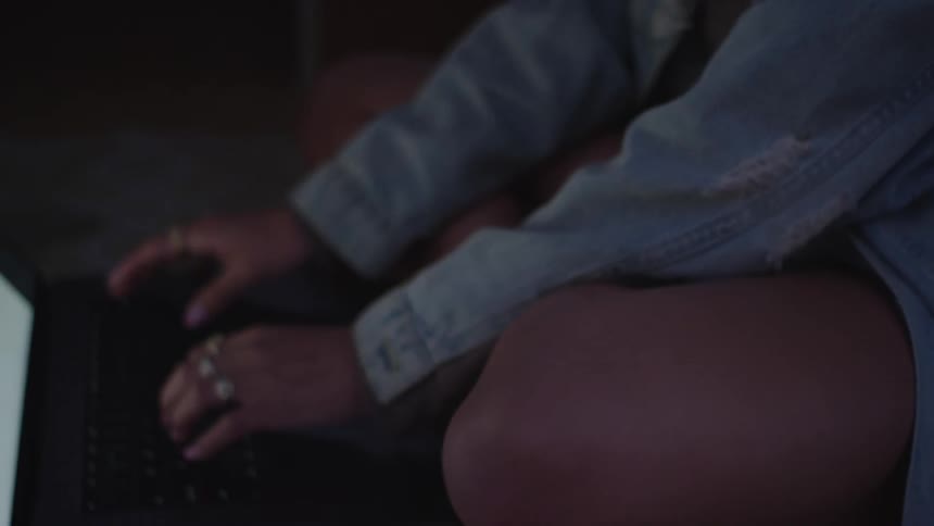 A woman sits in the dark and smiles as she types on her laptop