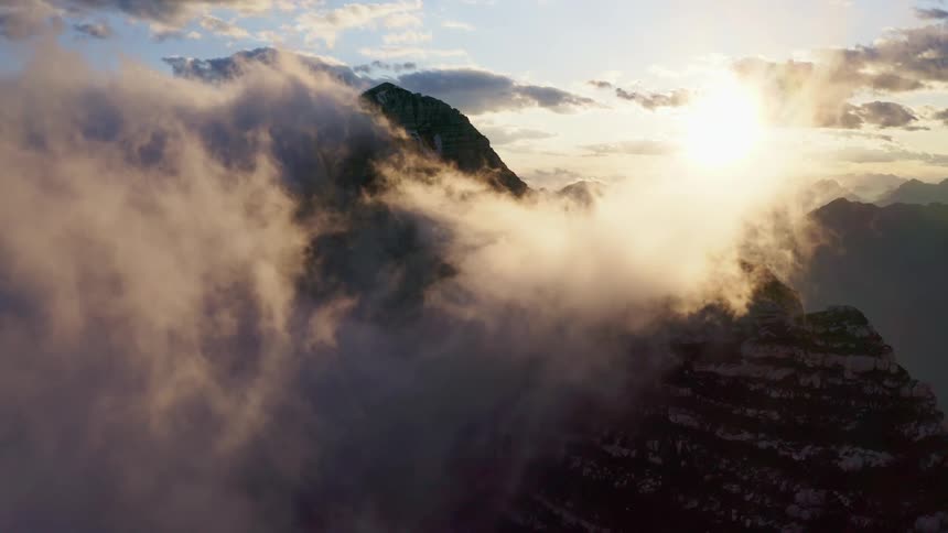 Aerial view of sunlight filtering throught the clouds over the snow covered steep cliffs on a mountain range at morning