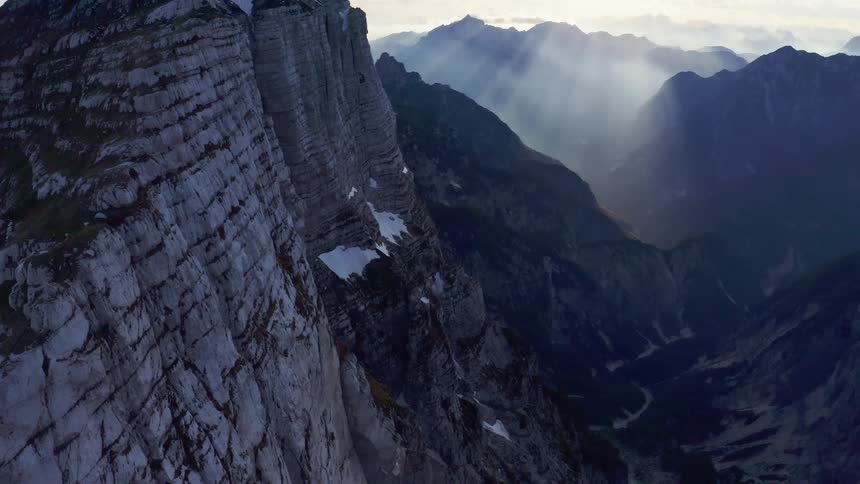 Sunlight filtering through the clouds over the snow covered steep cliffs on a mountain range at morning