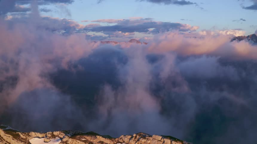 Clouds swirl over a snowy mountain ridge during the day