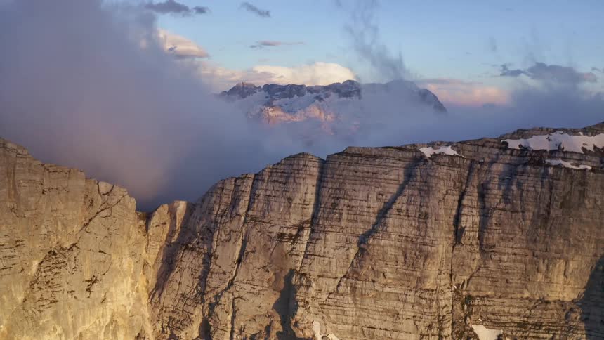 Aerial view of the snow covered steep cliffs on a mountain range under the clouds at morning