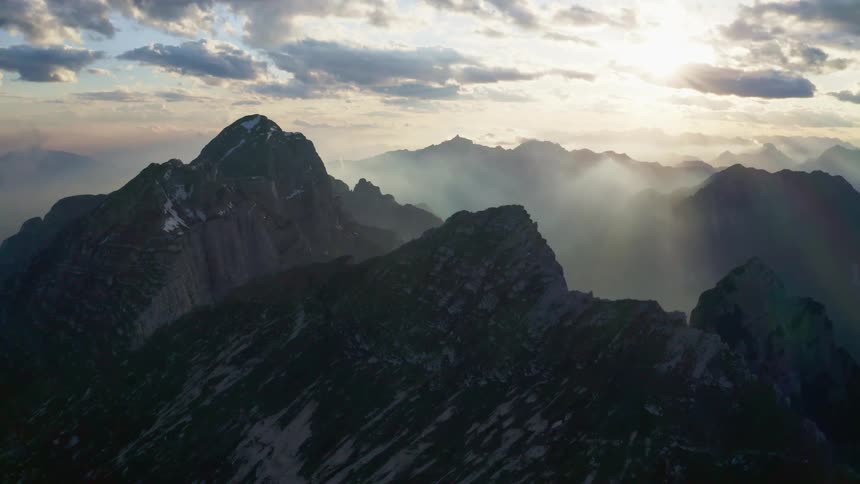 The sun peeks through clouds over a mountain range
