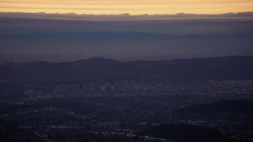 Lights shimmer and flicker from the city of Portland, Oregon with hills and mountains behind at sunset