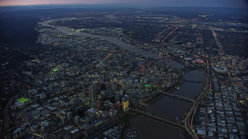 Super wide aerial of downtown Portland Oregon and the many bridges spanning the Willamette River as the camera flies high above the city in blue hour light after the sun has gone down