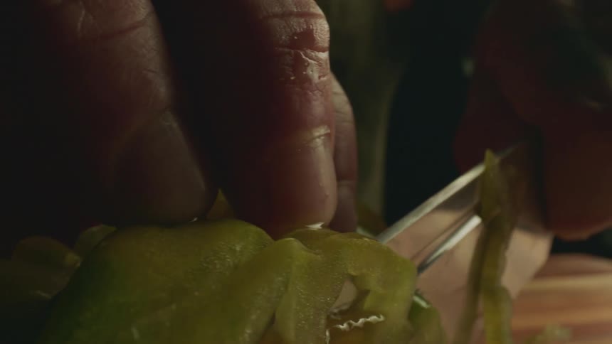 Close up of a tattoed man cutting green tomatoes with a sharp kitchen knife over a wooden board